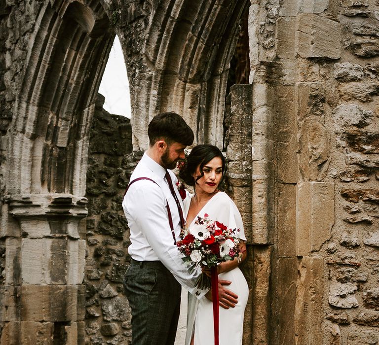 Bride and Groom with red and white flowers in churchyard ruins