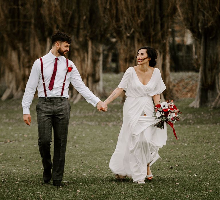 Bride and Groom walk hand in hand through gardens with white anemones bouquet