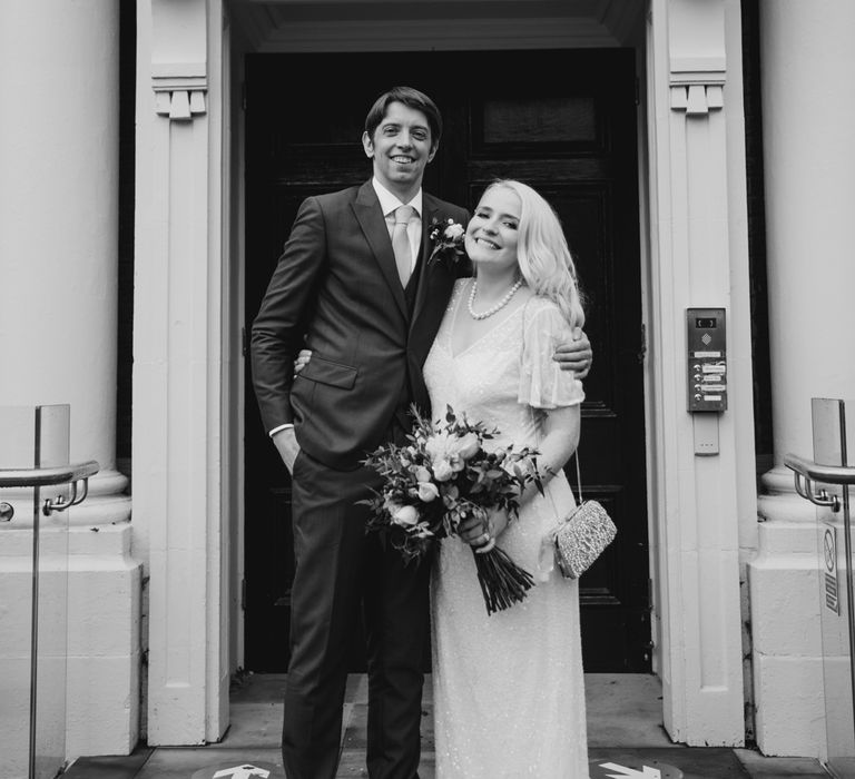 Bride & groom stand together outside door in black & white image