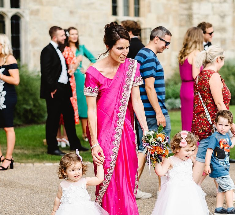 Bridesmaid in a fuchsia pink dress holding hands with the little flower girls outside the castle wedding venue 