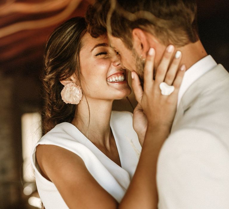 Beautiful bride with natural makeup and strapless bridal top holding her grooms face