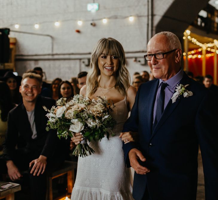 White blonde bride with fringe and bouquet walking down the aisle with her father