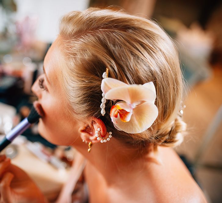 Bride to be applying makeup with peach wedding hair flower and pearl hair clip in her blode hair 