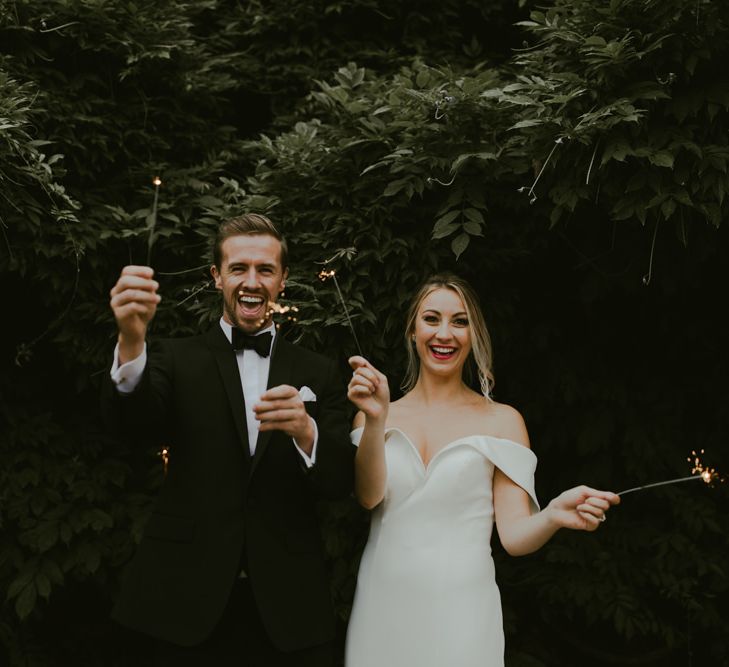 Bride & groom laugh whilst holding sparklers outdoors