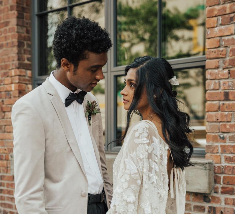 Groom in a grey blazer and bow tie holding his brides hand in a floaty boho wedding dress with embellished detail