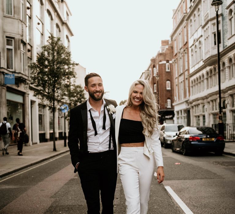 Bride & groom walk through London streets whilst bride wears white suit