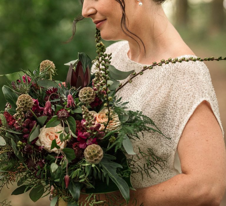 Bride smiles down whilst looking at floral bouquet