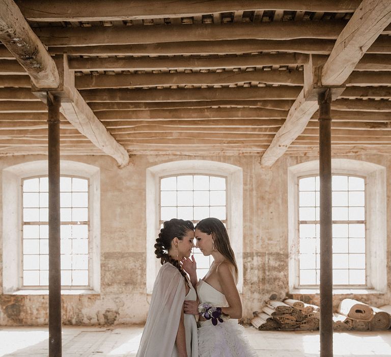 Stylish brides in a wedding cape and detachable ruffle skirt at their industrial wedding venue 