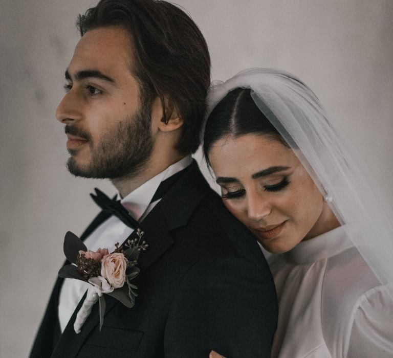 Bride leans into groom as they stand together for wedding photoshoot