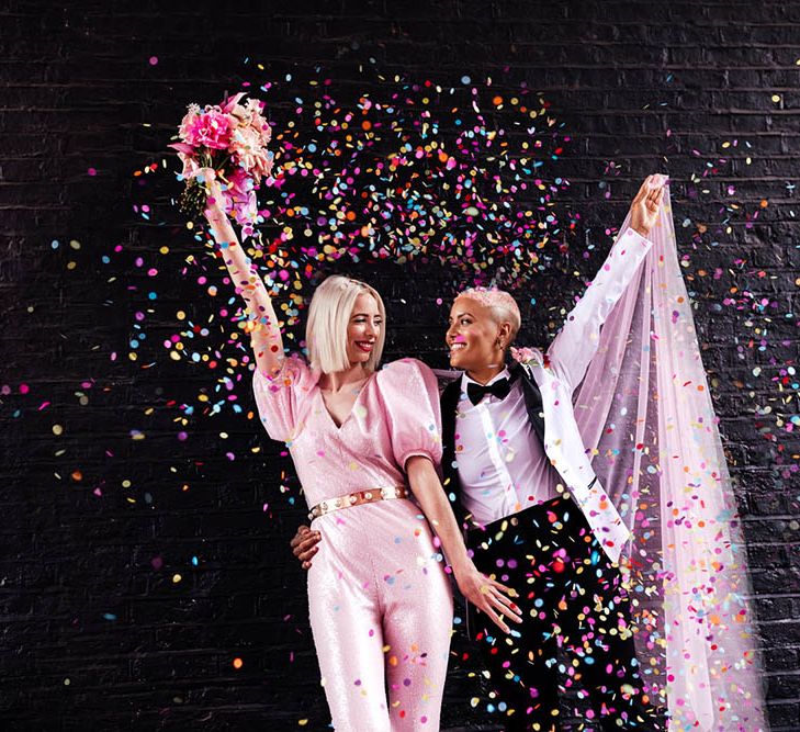 Confetti moment with bride in a fitted pink jumpsuit and white tuxedo jacket 