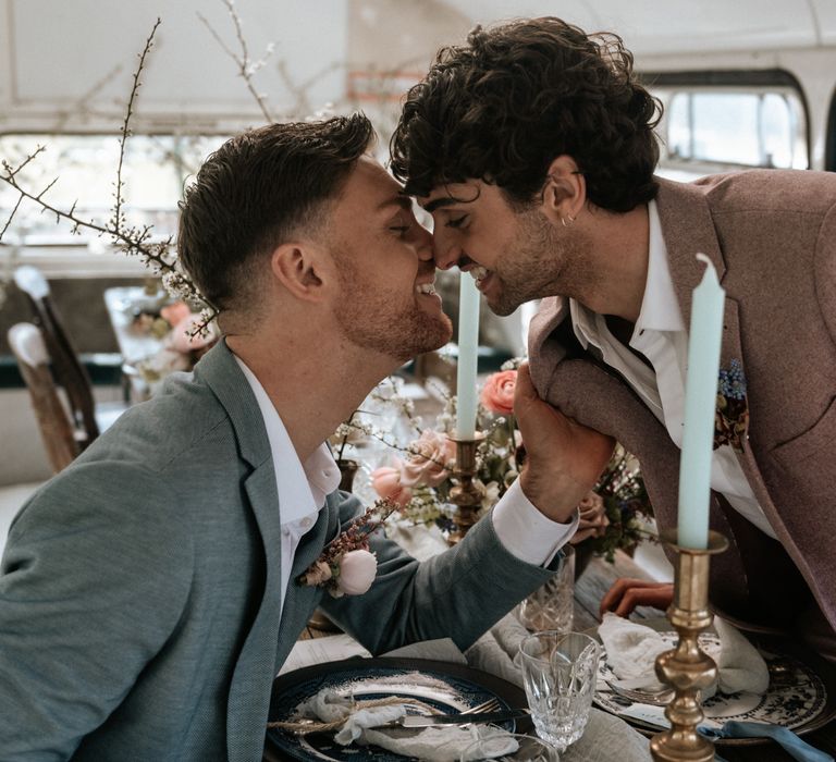 Groom leans across table to kiss groom on their wedding day