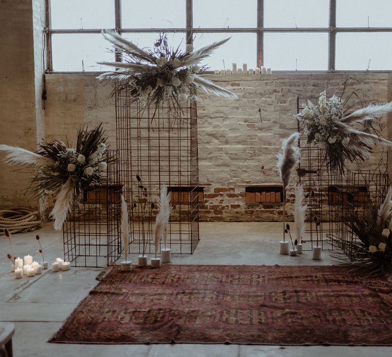 A wedding altar created rom wire frames and dried grasses and flowers. There is a red rub in front of the structure. 