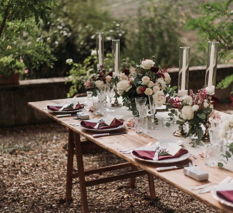 Table setting for Italian wedding with accent colour of red and wooden tables 