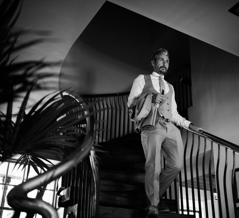 Groom in light brown Moss Bros suit walks down stairs at Hotel du Vin Harrogate holding jacket before Harrogate wedding