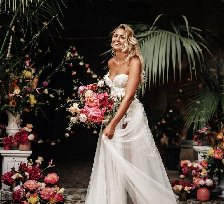 Bride with long flowing curls holding a pink bouquet and carrying her mesh split wedding skirt