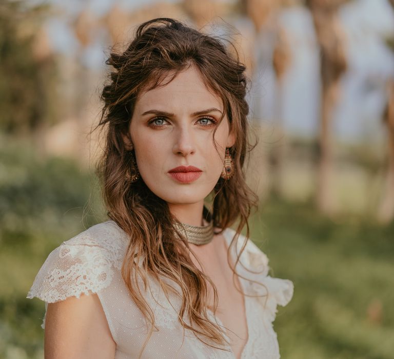 Beautiful hippie bride looks toward camera as she wears her brown hair in natural curls with minimalistic makeup and boho chic lace wedding gown 