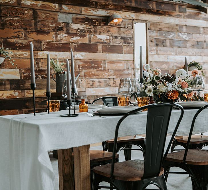 Industrial tablescape in a rustic wedding venue with black metal chairs and candlesticks orange glassware and white and orange flowers