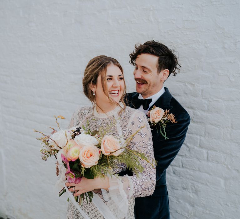 Groom wraps his arms around bride after wedding ceremony as they laugh with one another 