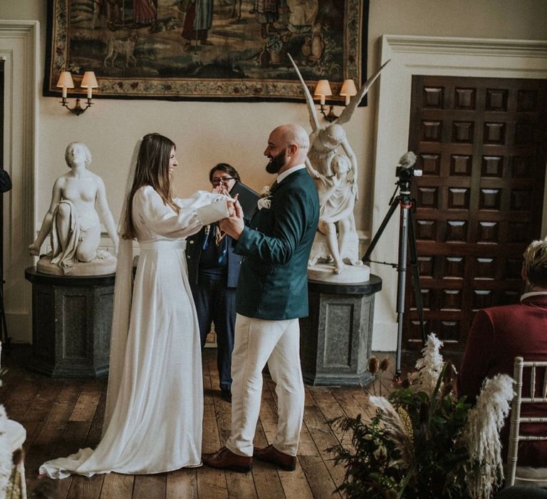 Bride & groom hold hands at the front of the aisle whilst laughing with one another 