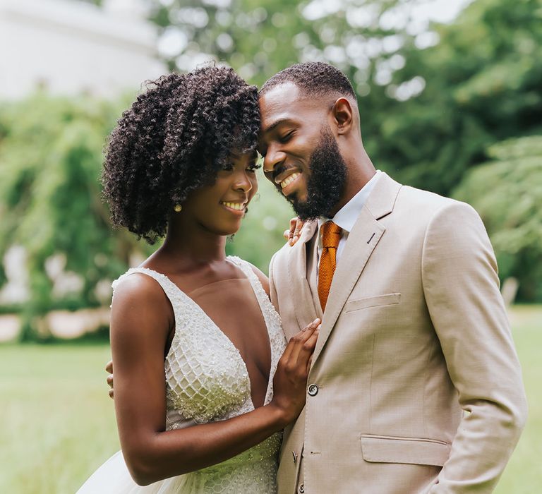 Intimate bride and groom portrait with groom in a beige suit and bride with afro hair in a plunging neckline wedding dress with embellished detail