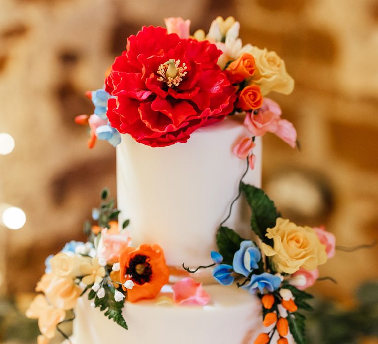 White three tier iced wedding cake with multicoloured floral decorations on wooden table at The Bridal Barn wedding reception