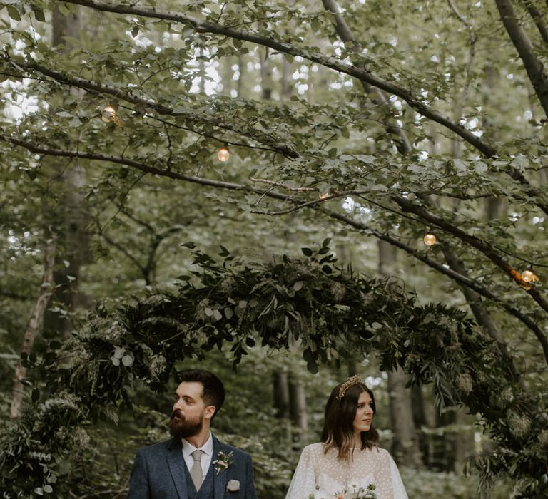 Bride & groom walk under archway covered in green foliage