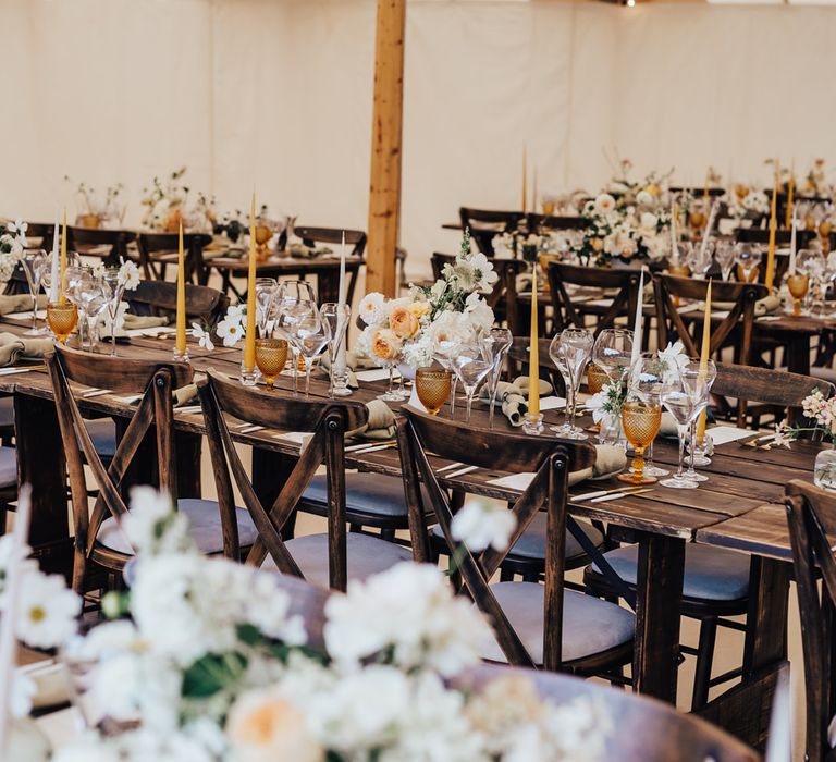 Interior of rustic sperry tent wedding reception with wooden tables, white and peach florals and amber glassware 