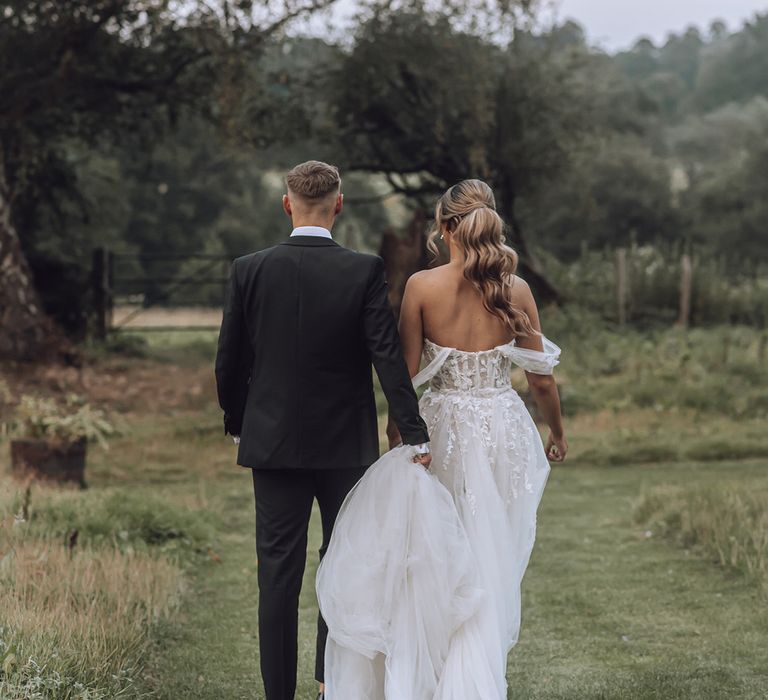 Bride & groom walk hand in hand across field on their wedding day