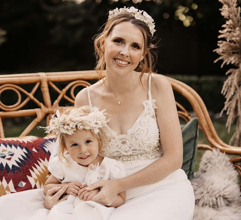 Bride sits with her daughter outdoors who wears dried floral crown