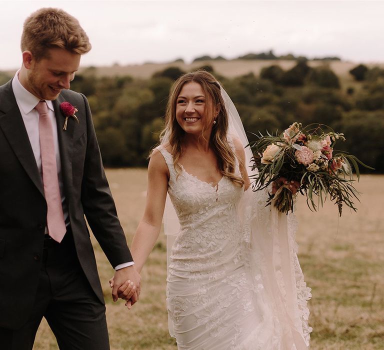 Bride in Pronovias wedding dress holds hands with Groom as she walks through White Pond Farm venue