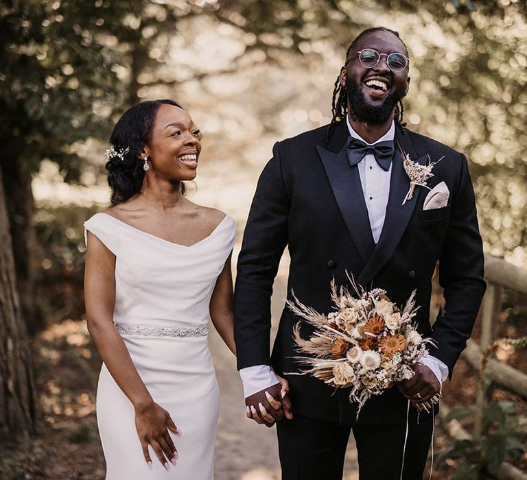 Bride & groom walk together as groom holds dried floral bouquet