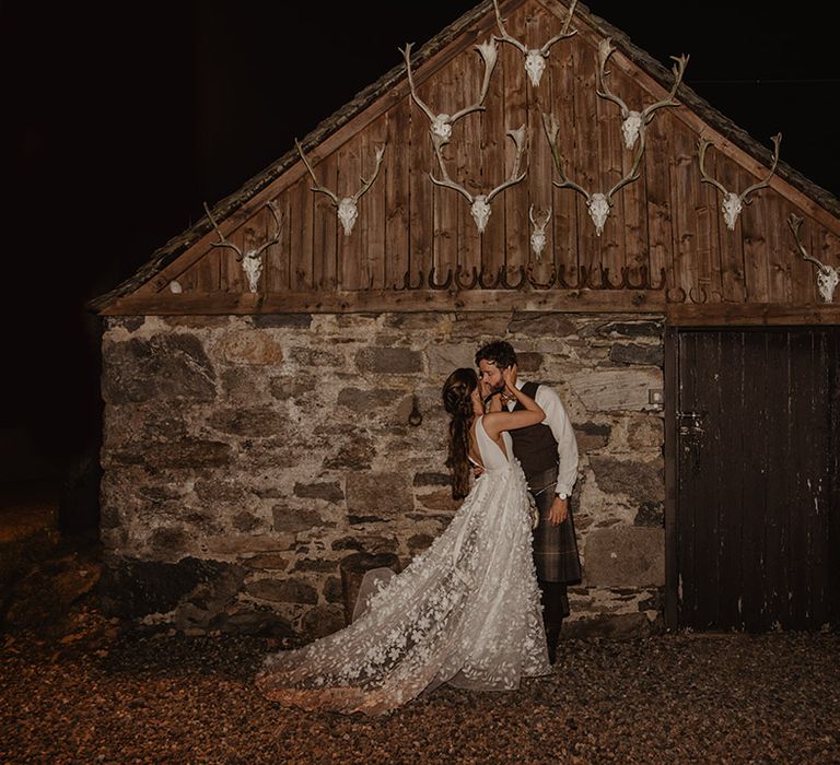 Bride in flower lace skirt wedding dress from Savin London kisses the groom in front of boathouse