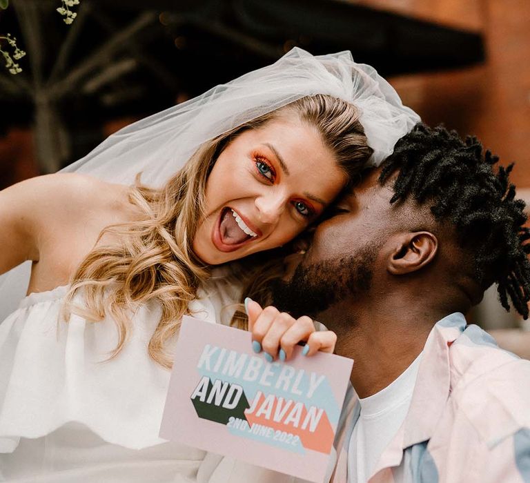 Bride in a short off the shoulder wedding dress holding a contemporary pastel wedding invitation