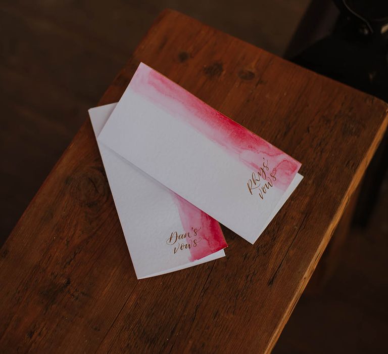 Pink and white vow booklets on wooden bench 