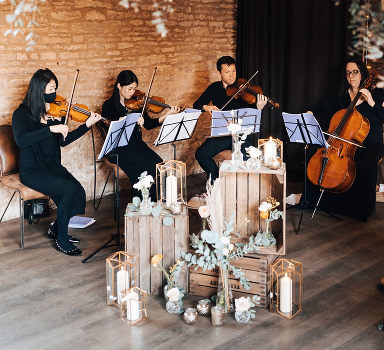 Live strings wedding entertainment band with rustic wooden crates and candles in lanterns with white and orange autumnal flowers 