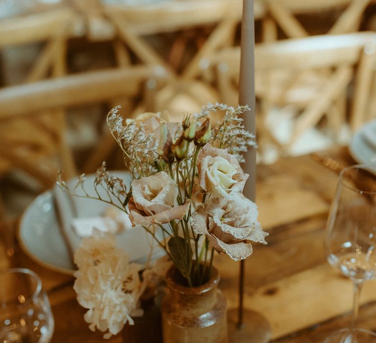 Wooden banquet table with small flower arrangement and grey tapered candle for table setting