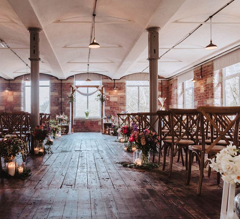 Bowers Mill ceremony room with aisle decorated with candles in glass vases and colourful flowers and a frame with wedding drapery at the altar 