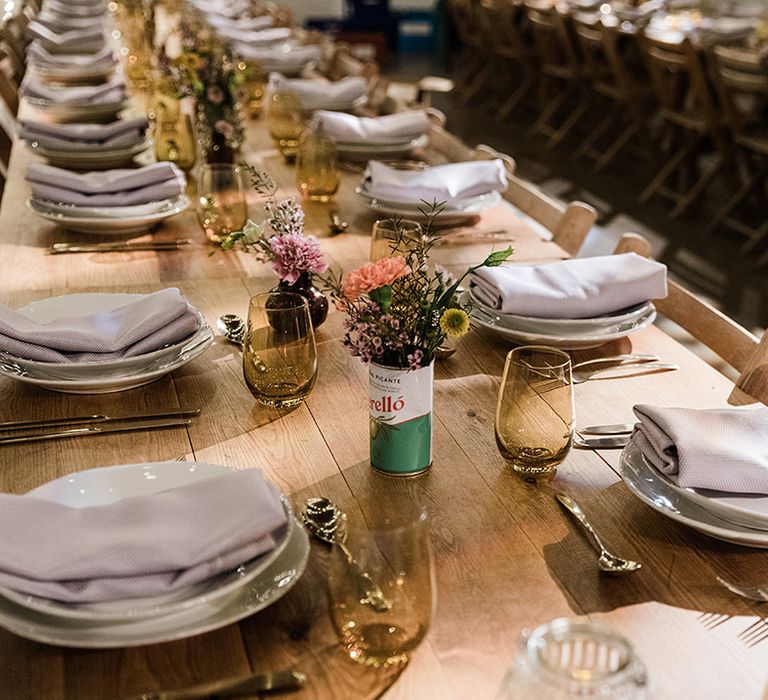 White plates with lilac napkins and coloured glassware for table setting decorations with tin can vases of flowers