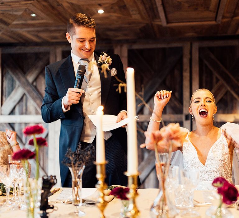 Groom in grey and black morning suit reads out his wedding speech with bride in lace wedding dress celebrating