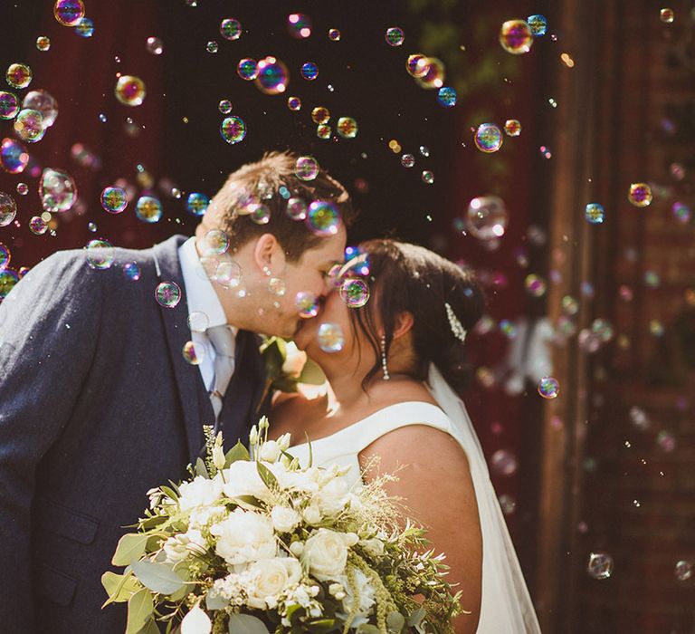 Bride and groom kiss as bubbles blow across the couple