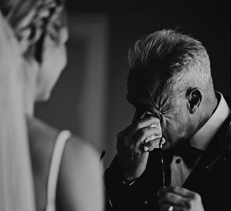 Father of the bride wipes his eyes as he sees the bride 