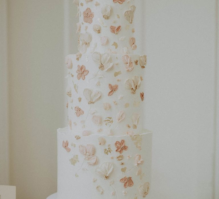 Three tier white frosted wedding cake with white, pale and dark pink flowers with gold flakes 