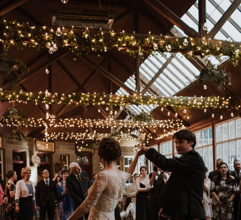 Groom in a kilt twirling his bride in a lace dress at Errol Park wedding venue with fairy lights wrapped around the beams 