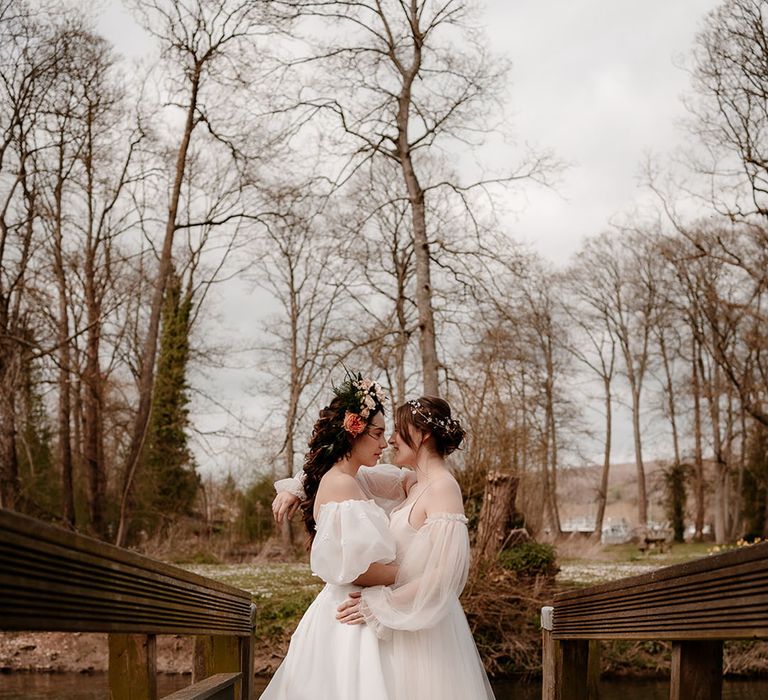 Two brides on the bridge at Mapledurham in ethereal wedding dresses with flower crown and hair vine bridal accessories 