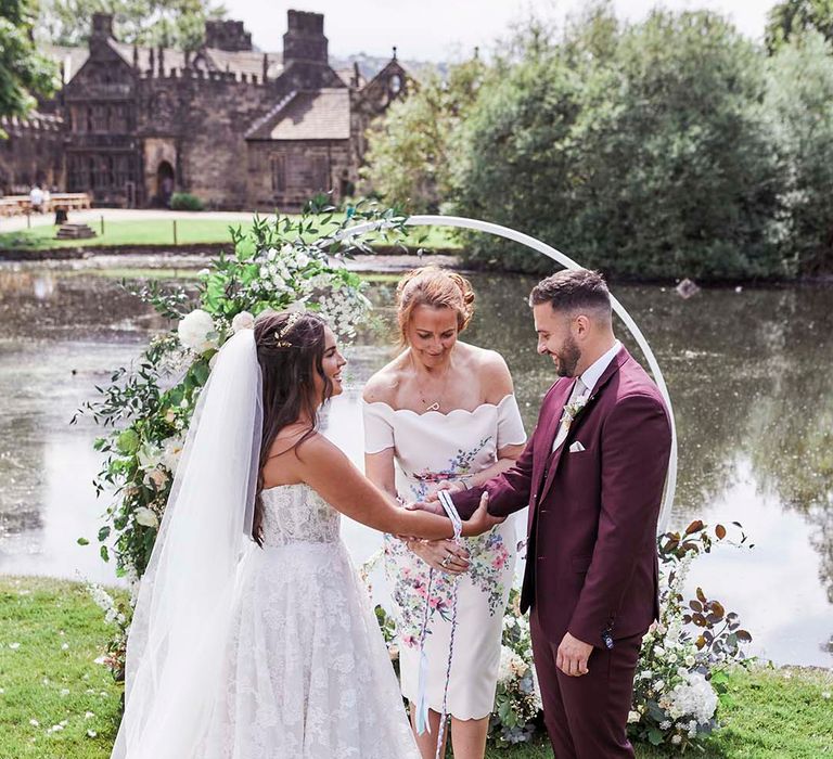 Celebrant led handfasting ceremony with bride in a lace Maggie Sottero wedding dress and groom in a burgundy suit 