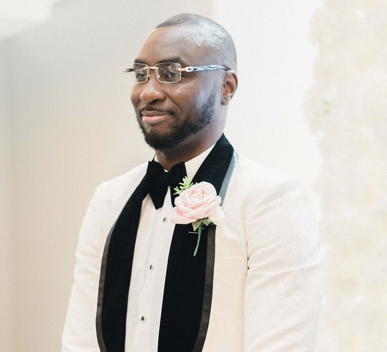 Groom wears white dinner jacket finished with black lapels and pale pink buttonhole 