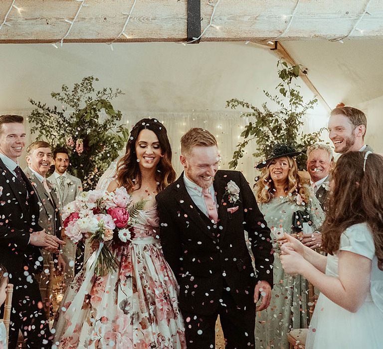 Bride and groom walk through pink and white round confetti after their wedding 