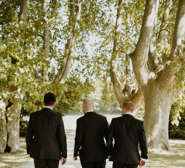 Groom walks with his groomsmen wearing black tie through grounds of Mas Loisonville in France