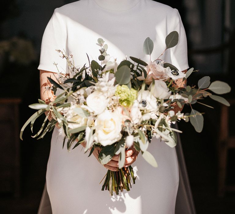 Bride with pearl drop earrings in a Jesus Peiro high neck wedding dress with pink and white flower bouquet 