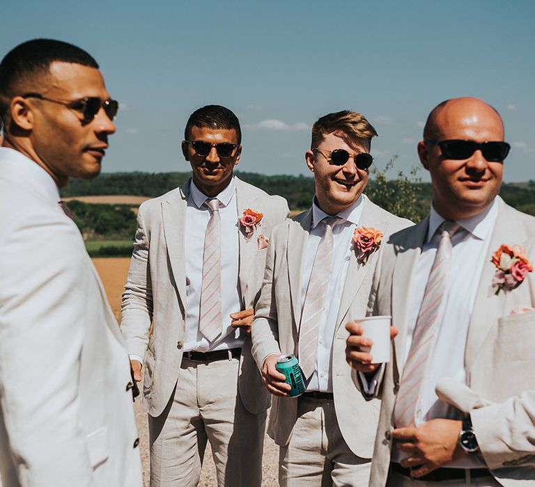 Groomsmen in sunglasses with cream suits, pink striped ties and pink flower buttonholes 